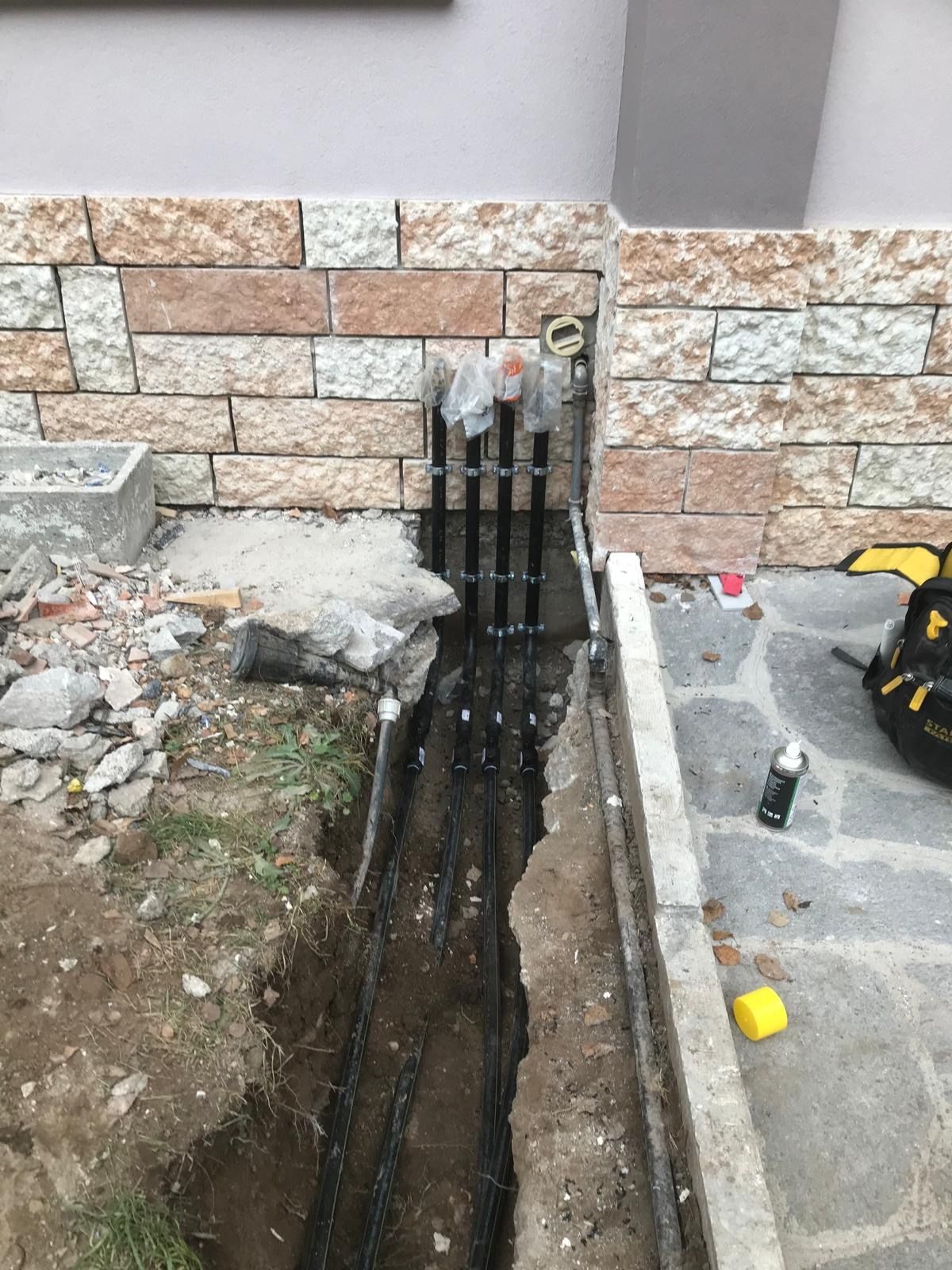 Quattro montanti gas in polietilene fissati con collari al basamento in pietra della casa, con le estremità protette e lo scavo ancora aperto